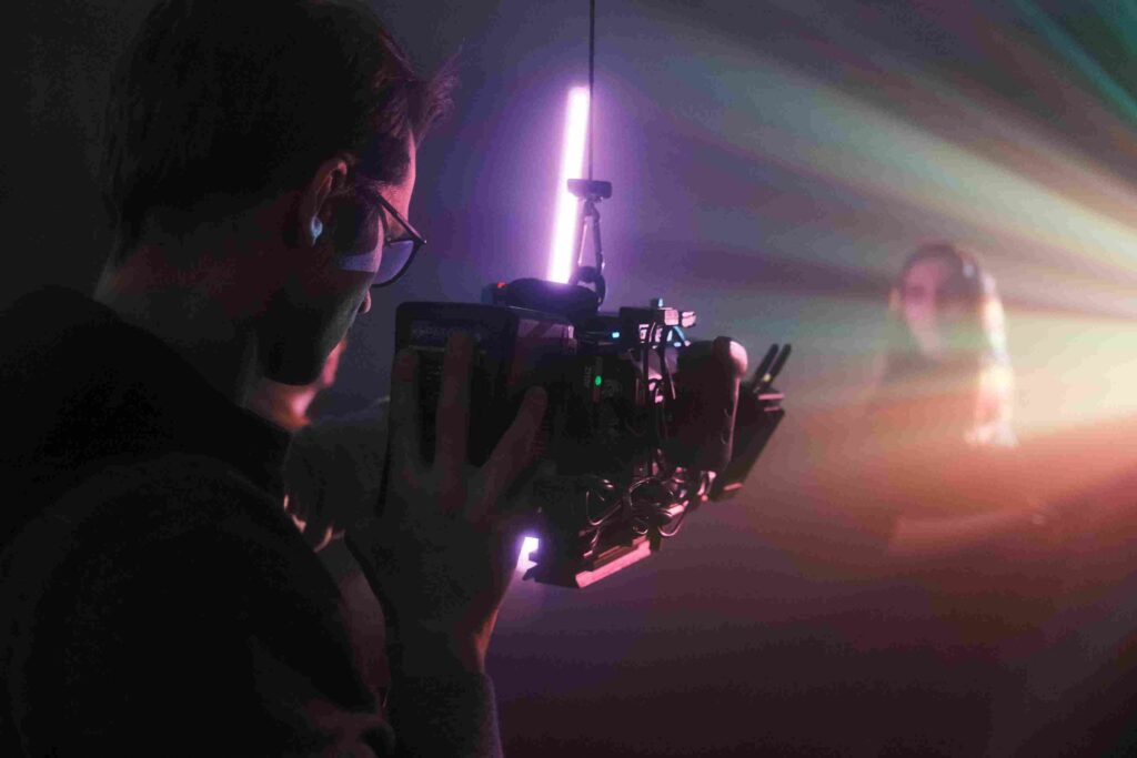 Kameramann filmt mit Handkamera eine Person bei violettem Neonlicht