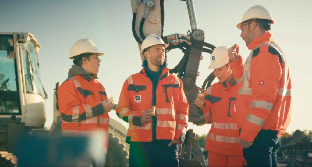 Bauteam der Sächsischen Bau GmbH in Warnkleidung vor einem Bagger