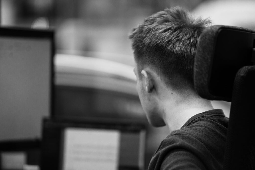 Person von hinten am Schreibtisch vor Monitoren, Schwarzweiß