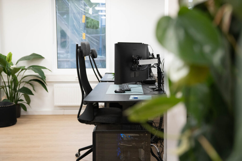 Schreibtisch mit Monitor, Bürostuhl und Kopfhörern zwischen Grünpflanzen