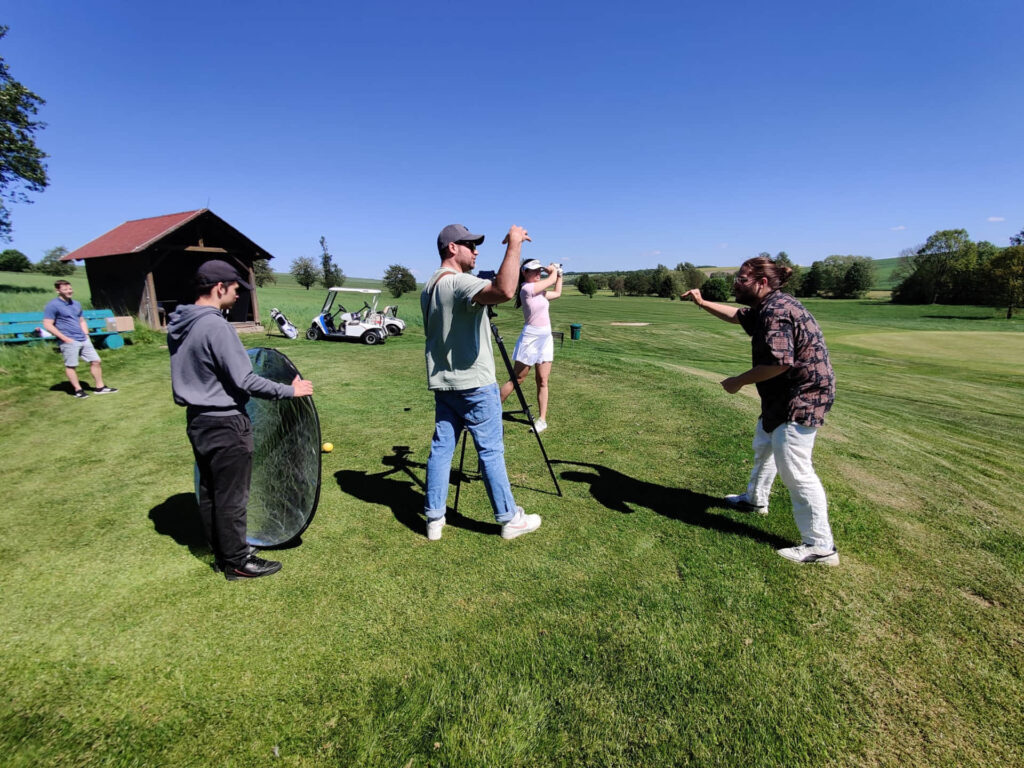 Crew mit Reflektor und Kamera auf Stativ dreht auf einem Golfplatz