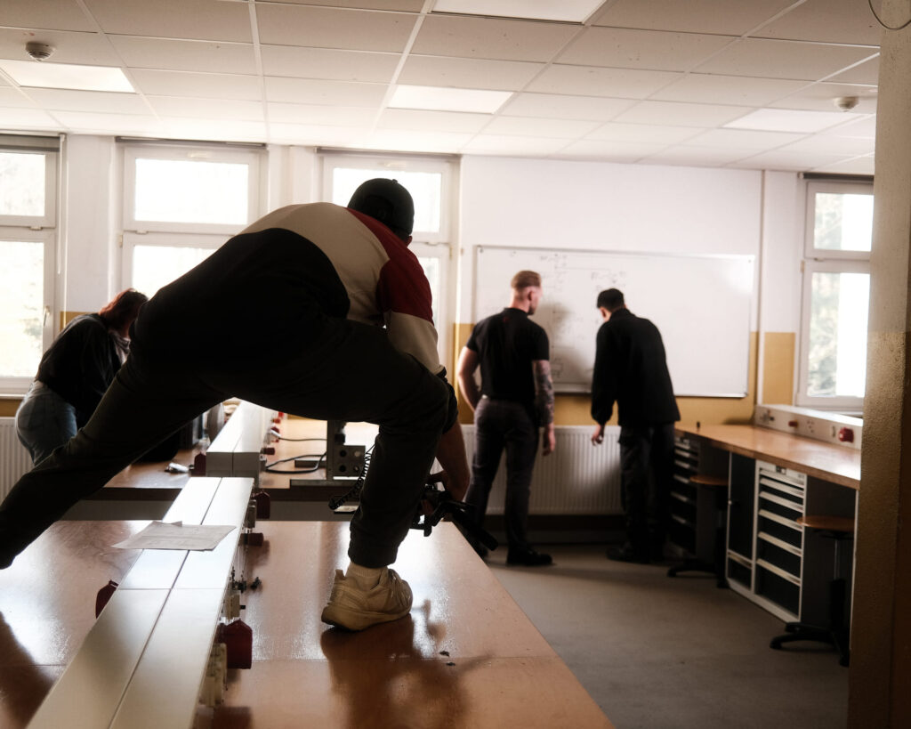 Kamerateam filmt zwei Mitarbeiter am Whiteboard in einer Werkstatt