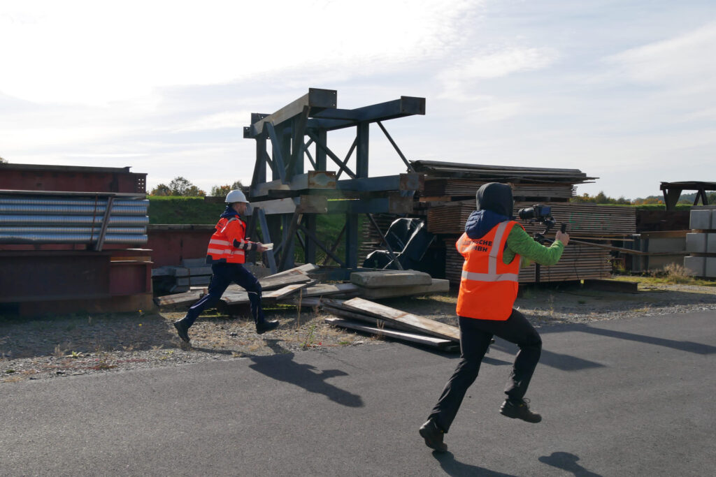 Videograf mit Gimbal filmt einen laufenden Bauarbeiter auf dem Gelände
